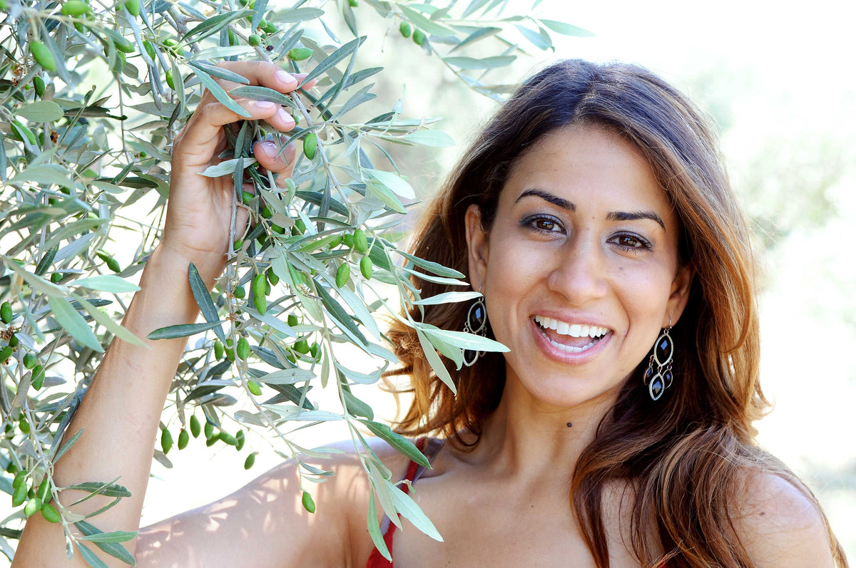 Claudia Hanna-Veysel, the founder of Olive Oil Flights, standing in an olive grove and smiling