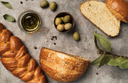 Various loaves of bread, a bowl of olive oil, and olives on a granite countertop